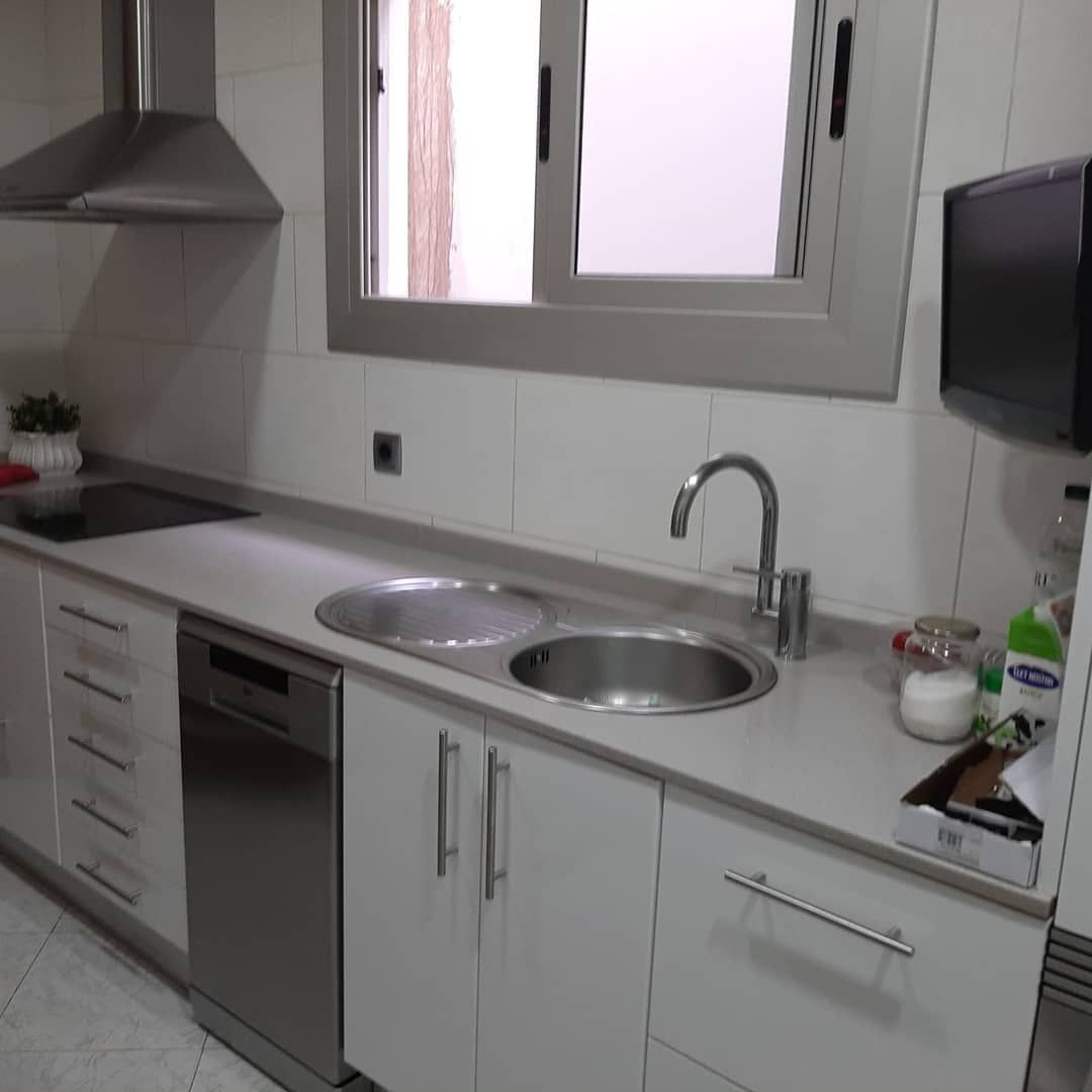 Cocina moderna con electrodomésticos de acero inoxidable, gabinetes blancos y un fregadero debajo de una ventana.