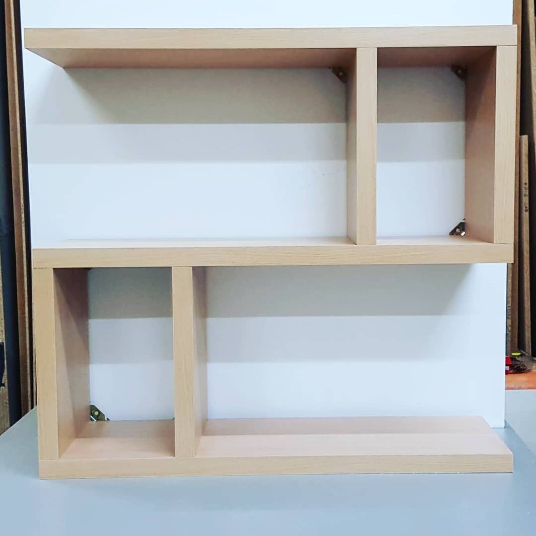 Estantería de pared de madera clara con un compartimento rectangular y dos cuadrados sobre una pared blanca.