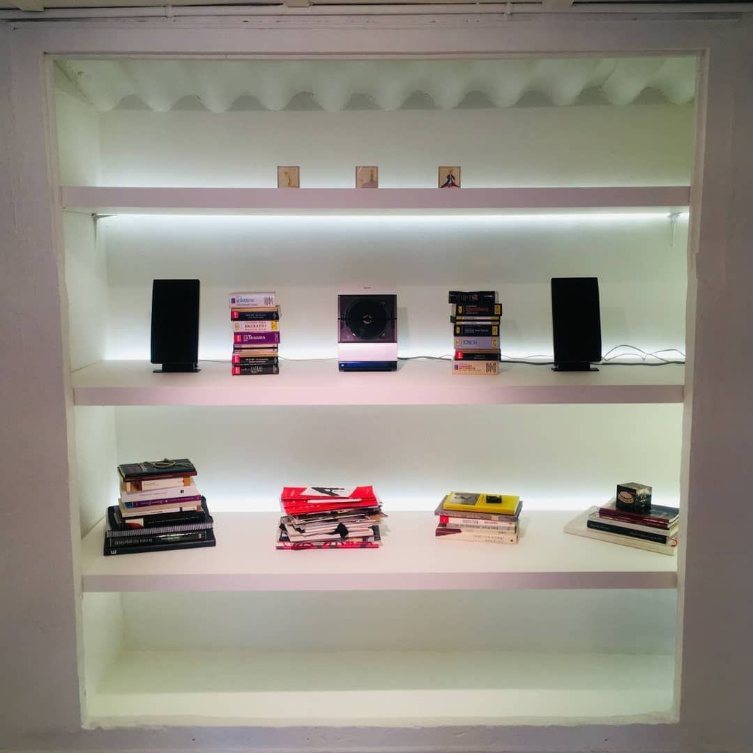 Estantes empotrados blancos con libros y altavoces. Iluminación superior e inferior.