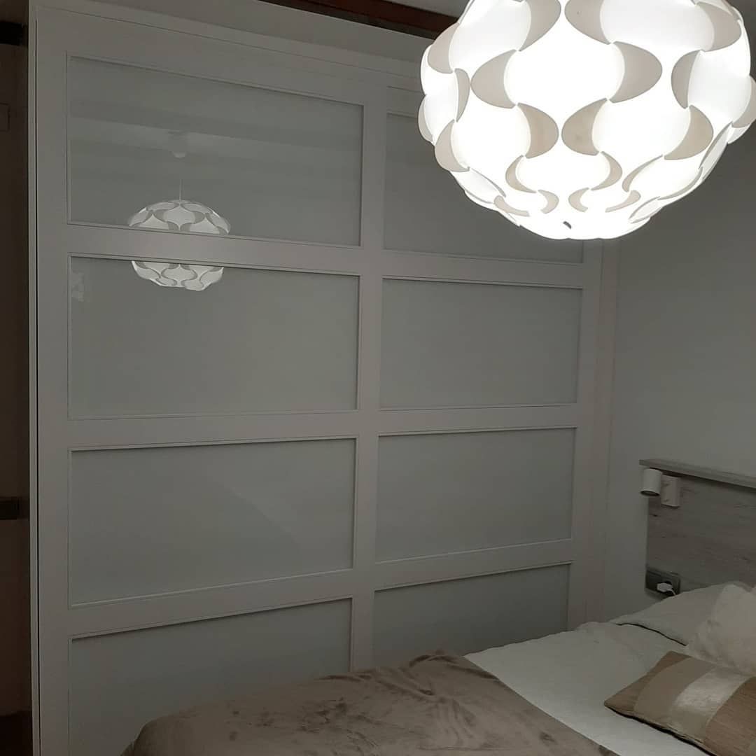 Puertas de armario blancas con paneles, al lado de una cama y una lámpara de techo estampada.