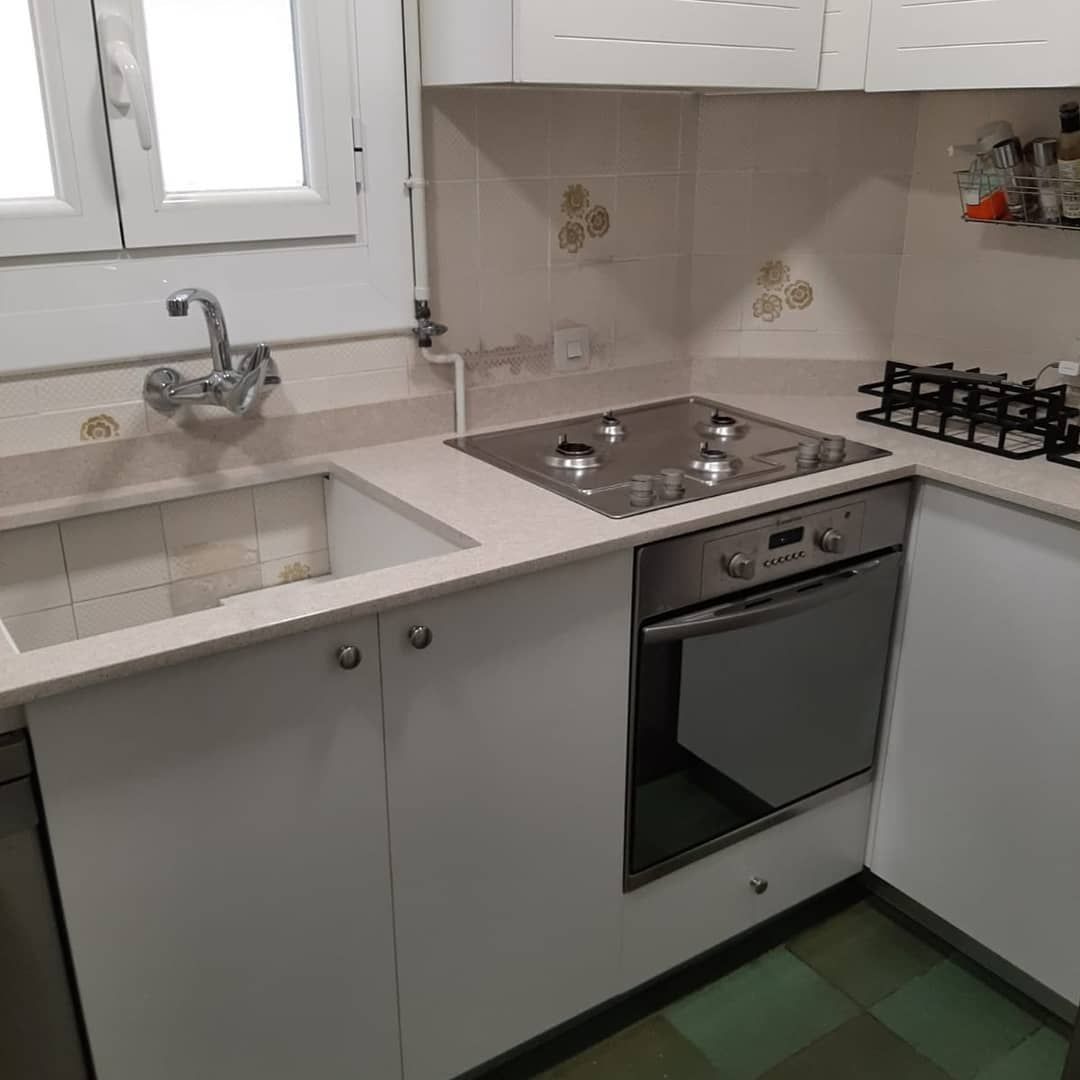 Cocina blanca con fregadero, vitrocerámica, horno y ventana.