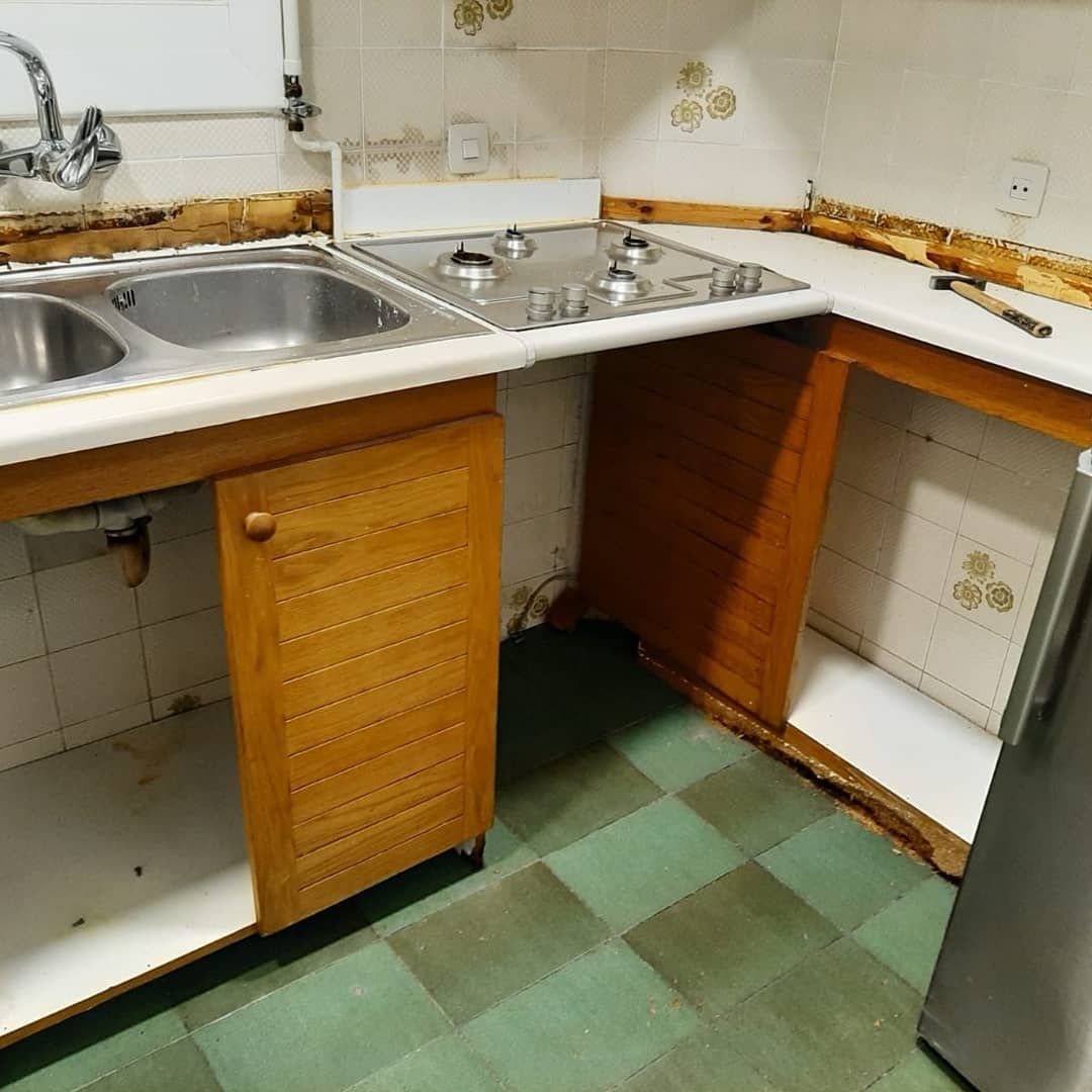 Una cocina parcialmente renovada con fregadero, estufa y gabinetes abiertos; azulejos verdes y blancos.