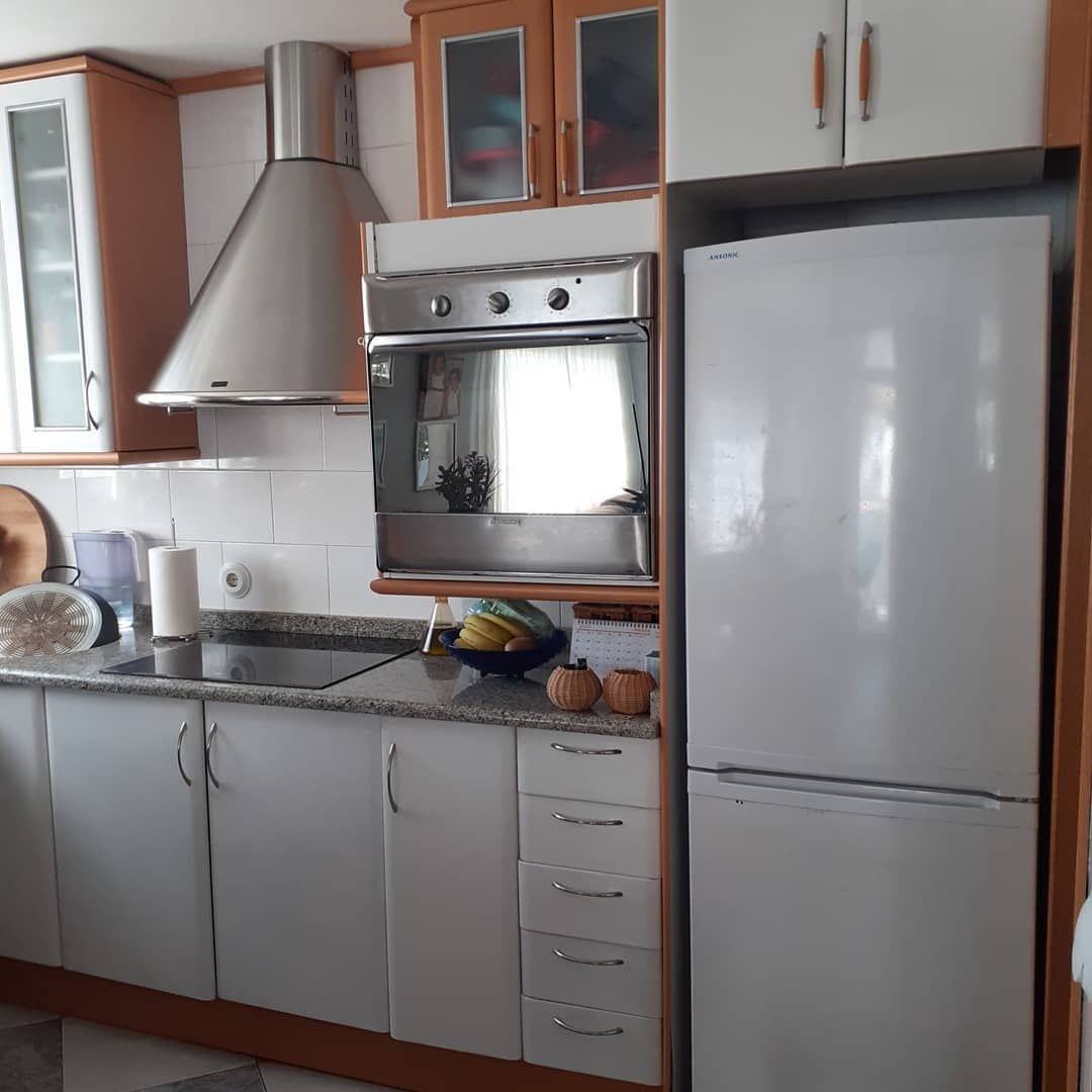 Cocina con gabinetes blancos, electrodomésticos plateados y encimeras de colores claros.