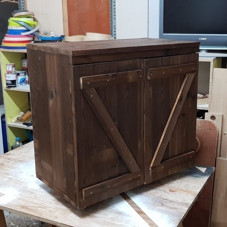 Armario de madera con dos puertas, teñido en marrón oscuro. Diseño de puerta estilo granero con refuerzos diagonales.