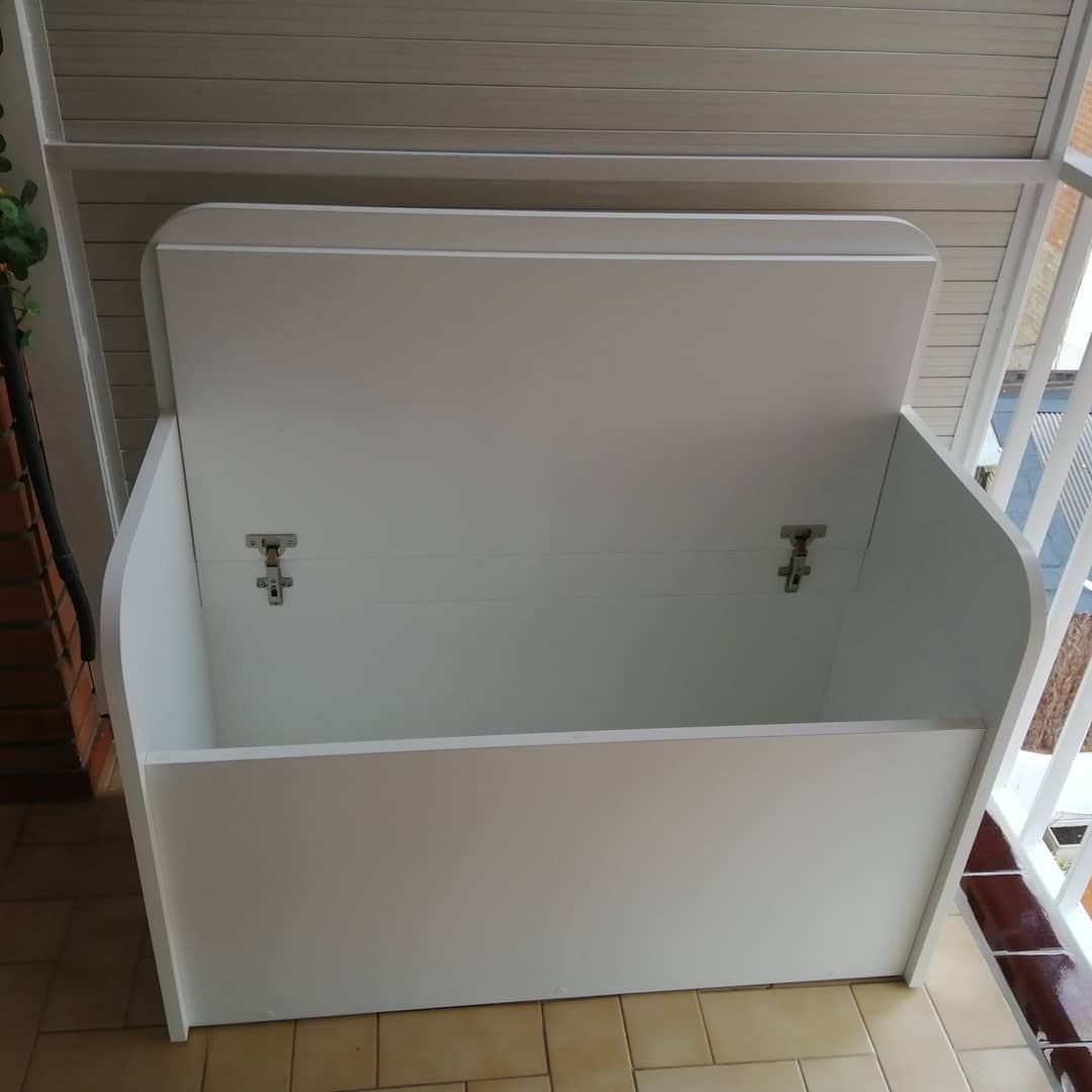 Caja de almacenamiento de madera blanca con tapa abierta en un balcón de azulejos.
