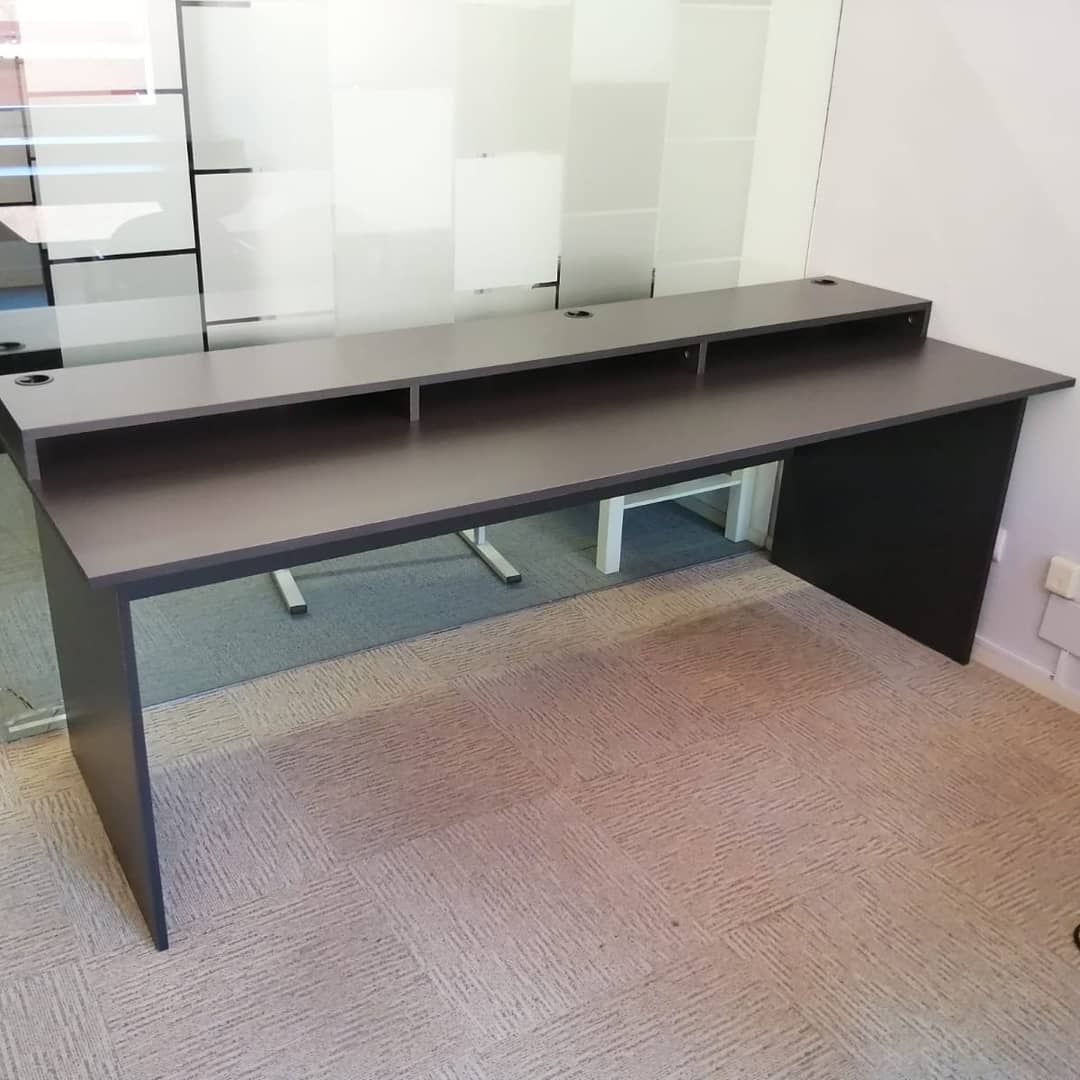 Escritorio gris oscuro con estante elevado, dos orificios para cables, en una habitación.