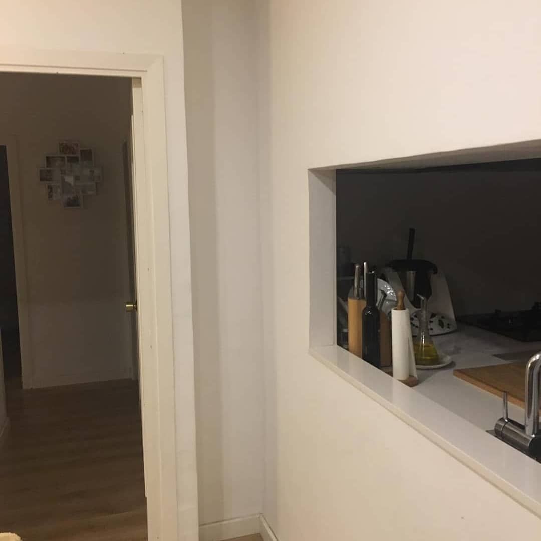 Vista interior con una puerta abierta a la izquierda y una ventana de paso a la cocina a la derecha.