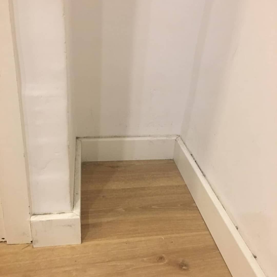 Paredes blancas, molduras y piso de madera clara en una esquina.