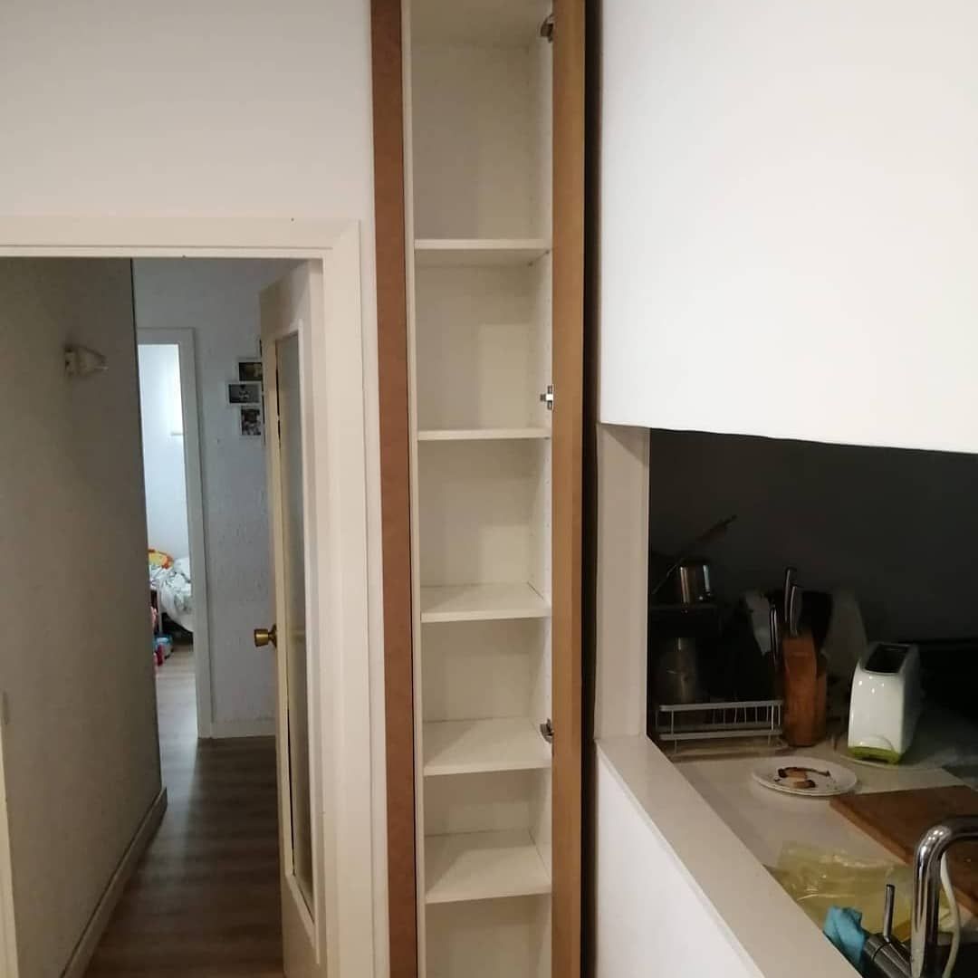 Armario alto y estrecho con puerta abierta, con estantes blancos.