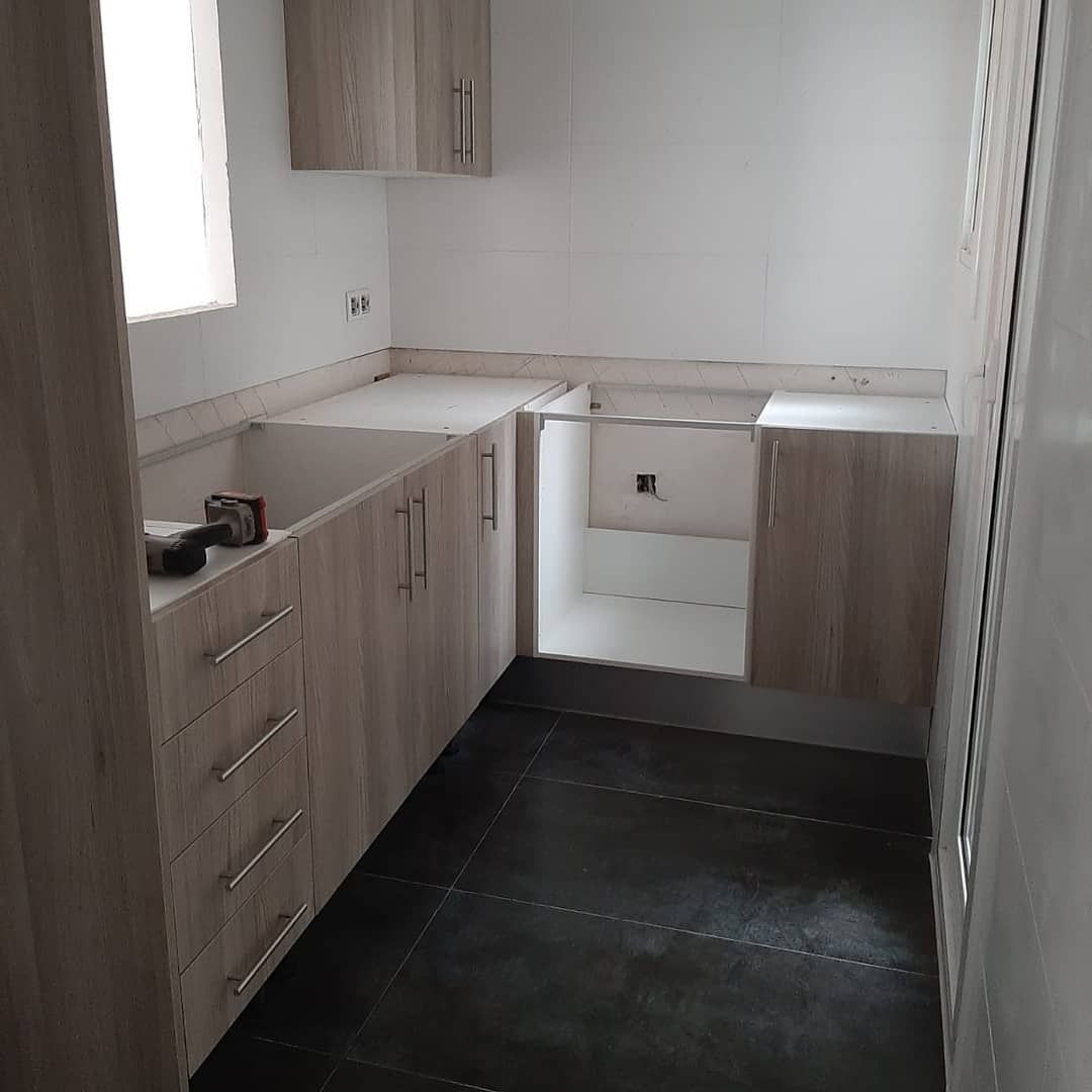 Cocina con gabinetes de madera clara, encimeras grises y piso de baldosas oscuras.