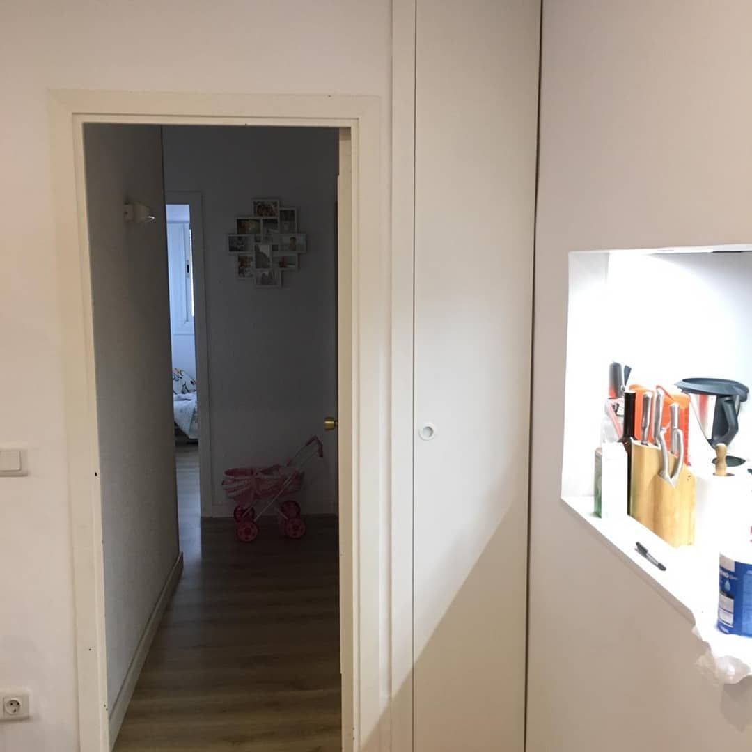 Pasillo interior con puerta que da a otra habitación. Se ve un cochecito de juguete. Paredes blancas.