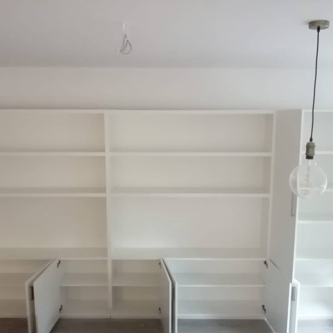 Estanterías y armarios empotrados blancos en una habitación. Una bombilla cuelga del techo.