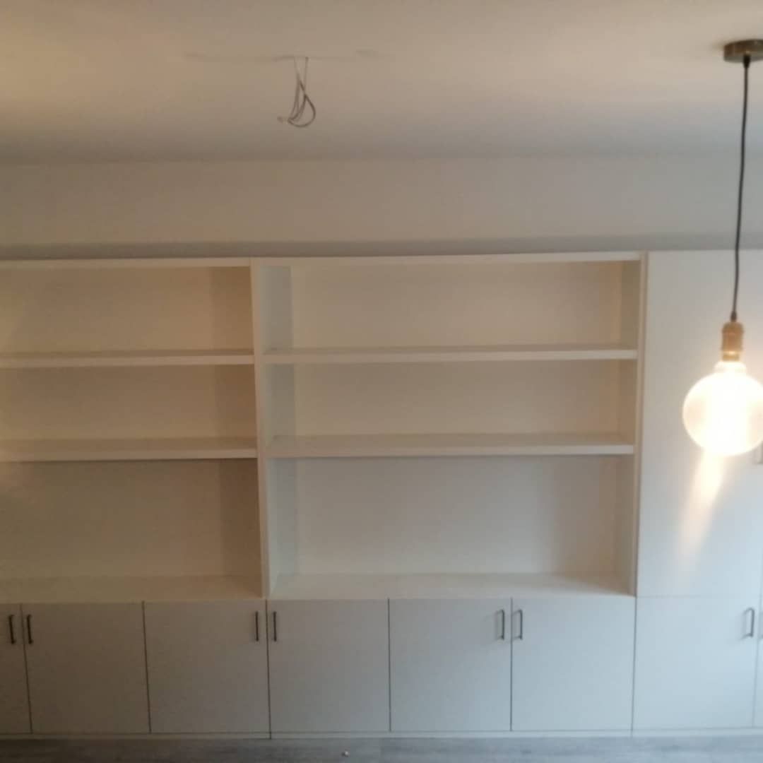 Estantería empotrada de color blanco con armarios, centrada bajo una lámpara de techo.