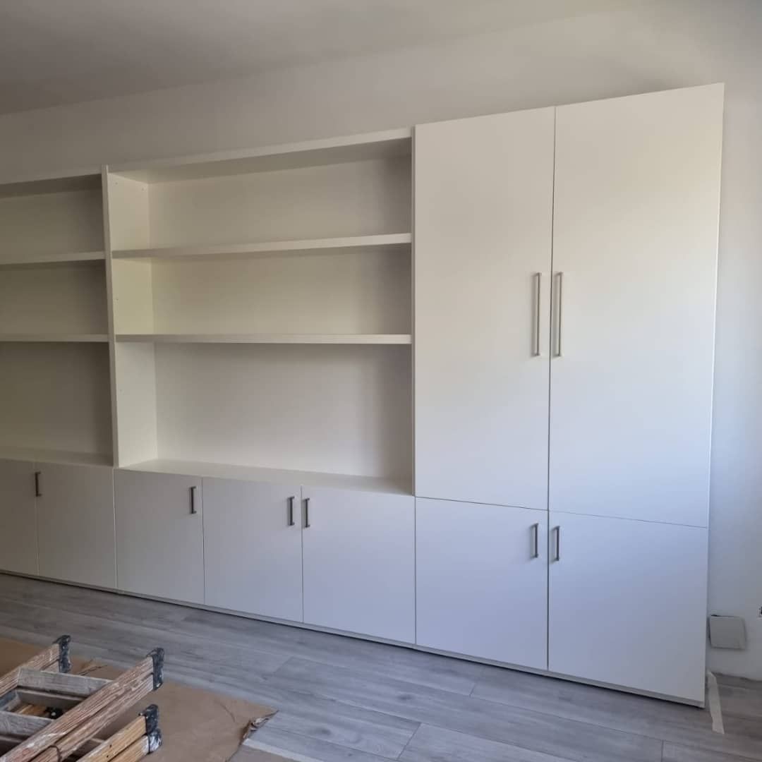 Unidad de almacenamiento blanca empotrada con estantes, gabinetes y puertas en una habitación.