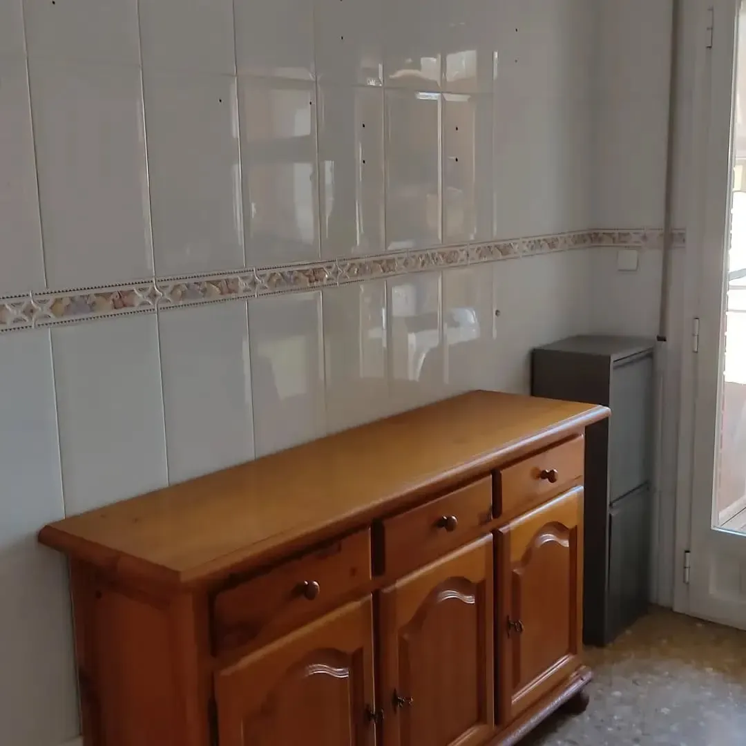 Un armario de madera contra una pared de azulejos. Junto a él hay un pequeño electrodoméstico.