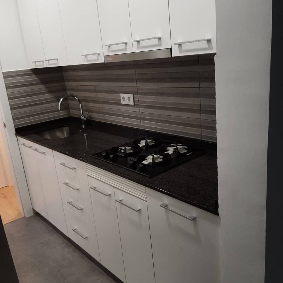 Gabinetes y encimeras de cocina blancos, con estufa y fregadero, protector contra salpicaduras gris.