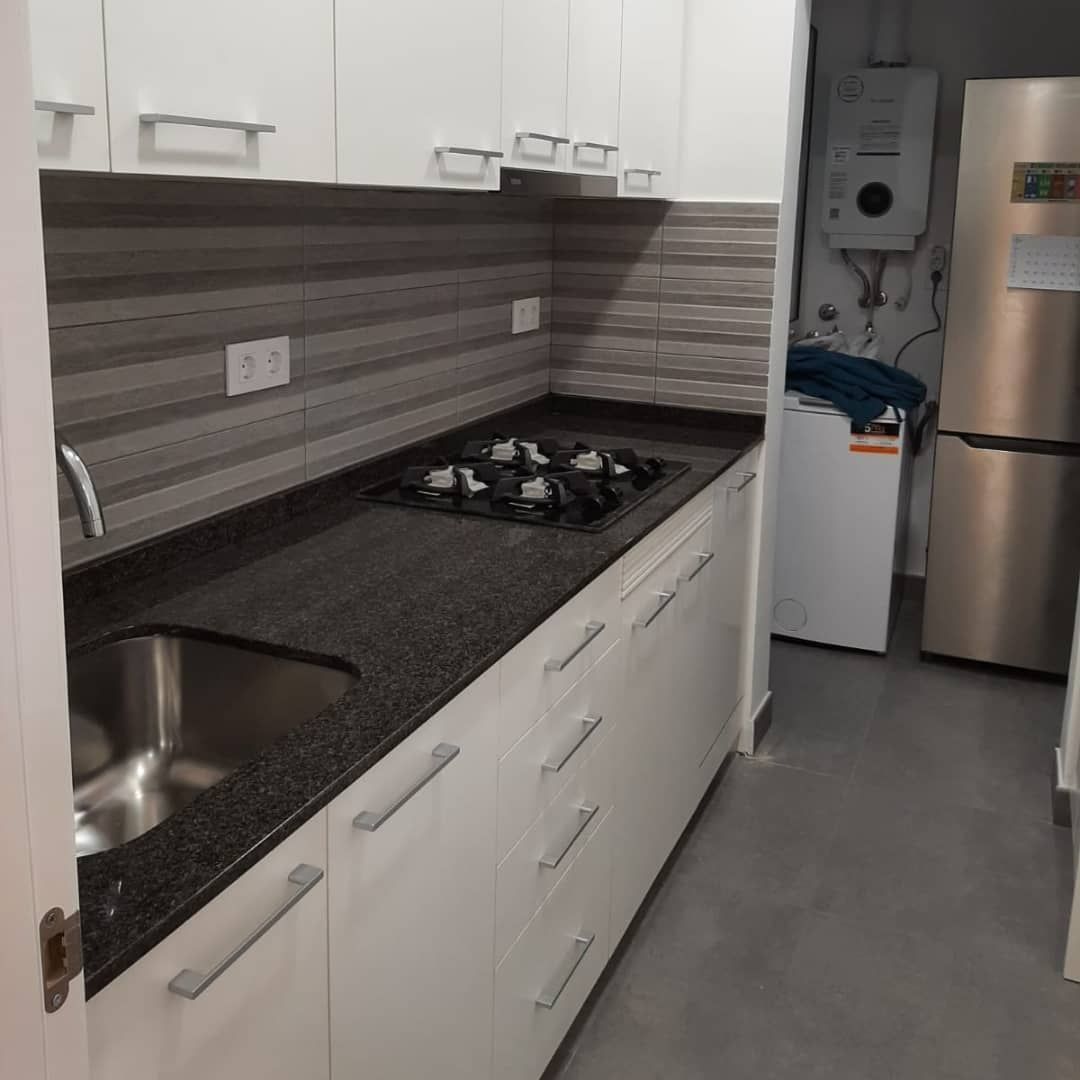 Cocina blanca con electrodomésticos de acero inoxidable, encimeras oscuras y estufa.