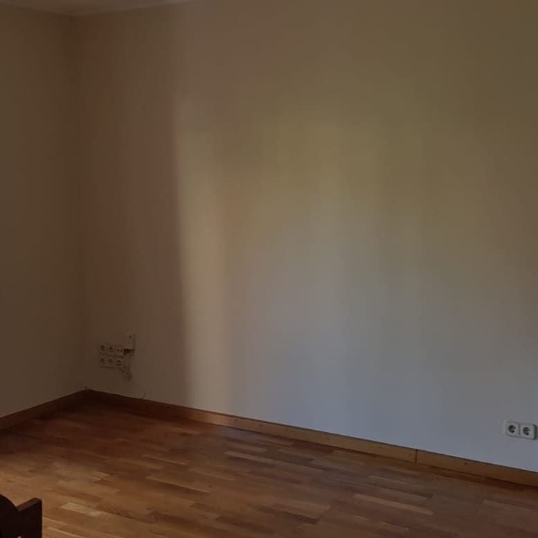 Habitación vacía con piso de madera y paredes beige, dos enchufes eléctricos visibles.