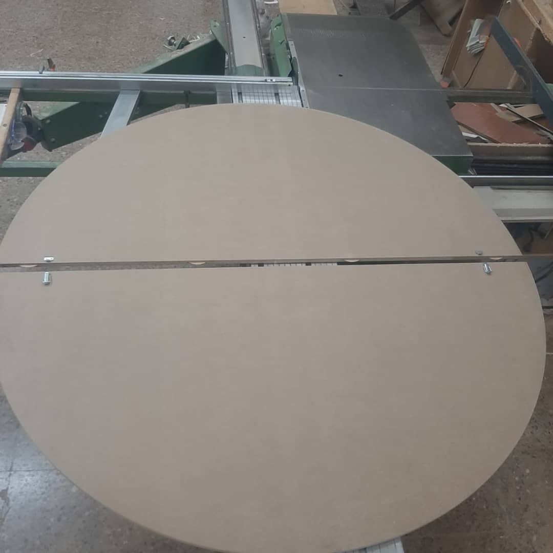 Tablero grande de color canela y circular, dividido en dos piezas, sobre mesa de carpintería.