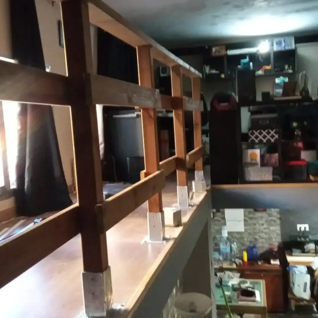 Barandilla de madera en buhardilla con vistas a estancia con muebles y electrodomésticos.