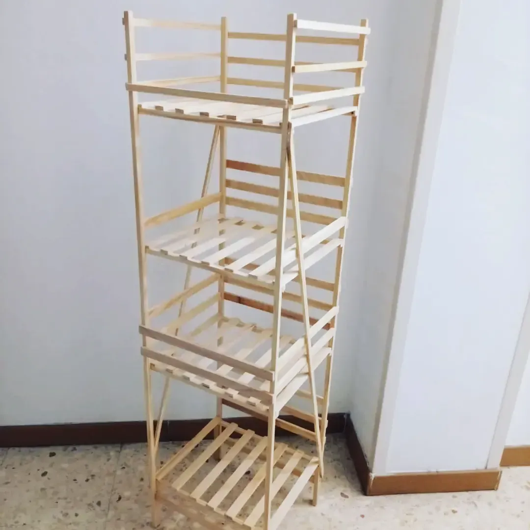 Estantería de madera de cuatro niveles con estantes de listones y una barandilla superior, apoyada contra una pared blanca.