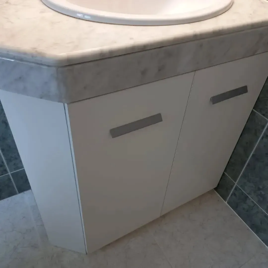 Mueble de baño blanco con encimera gris y tiradores plateados, diseño en ángulo.