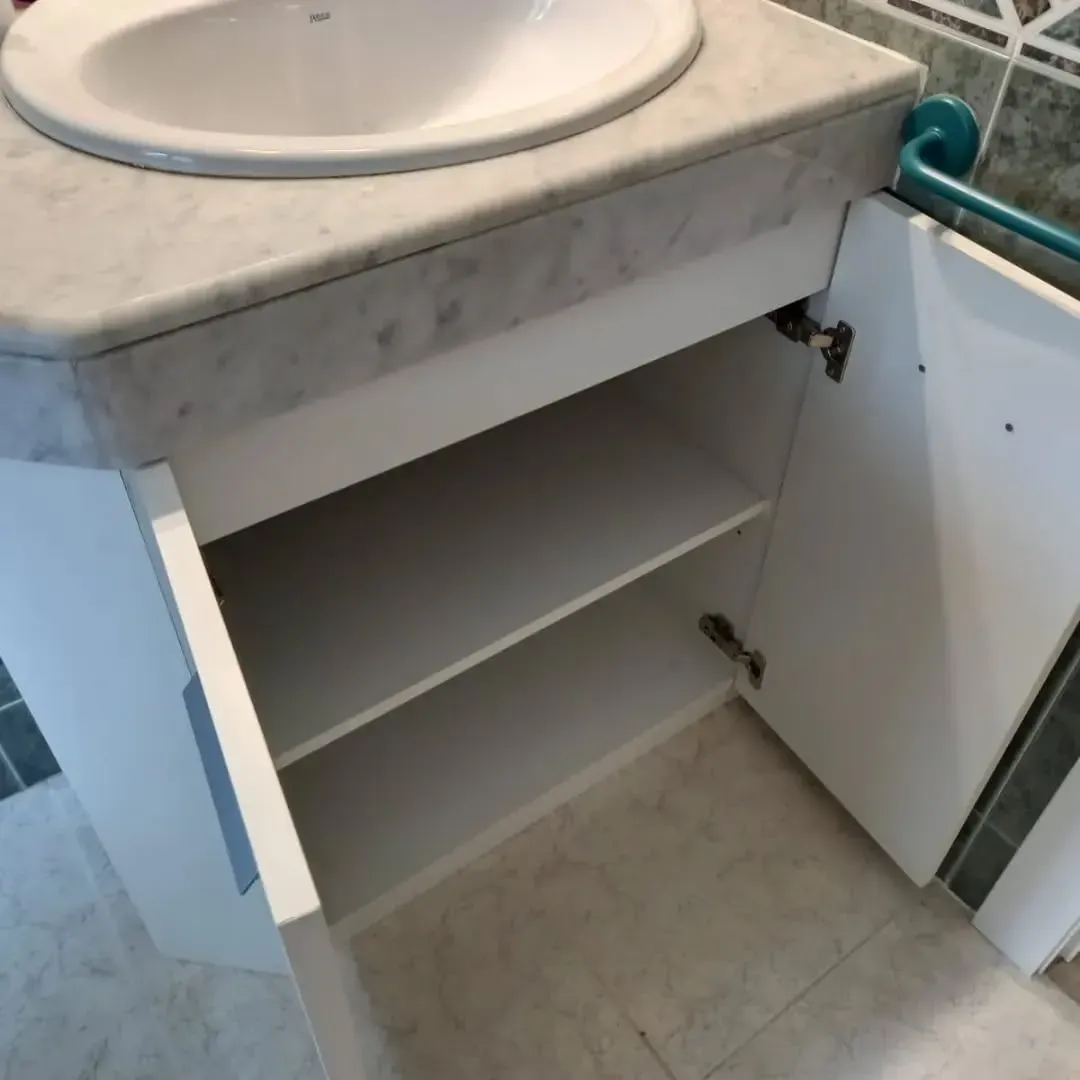 Mueble de baño blanco con puertas abiertas, dos estantes, encimera de mármol y lavabo.
