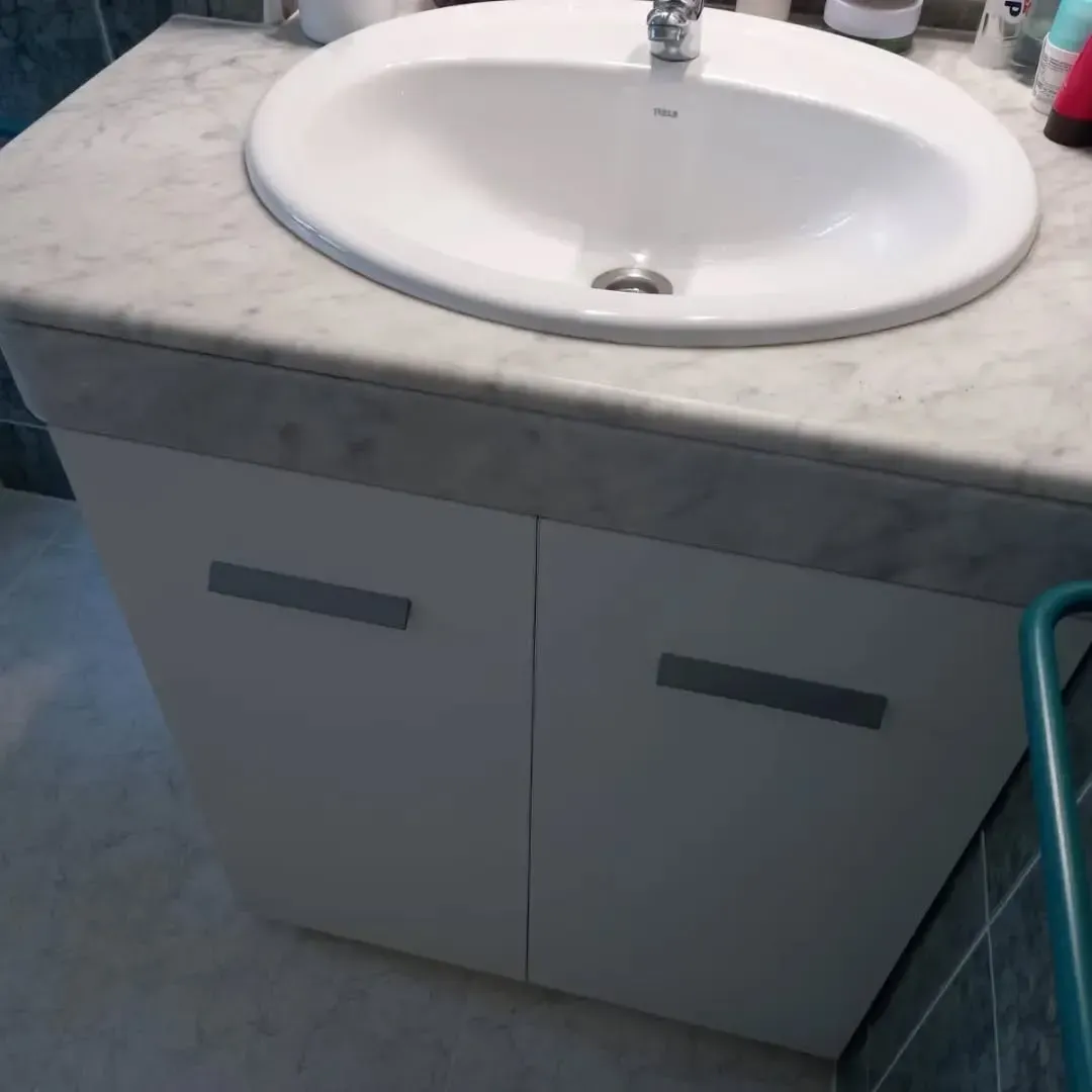 Mueble de baño blanco con lavabo ovalado, puertas blancas y encimera de mármol.