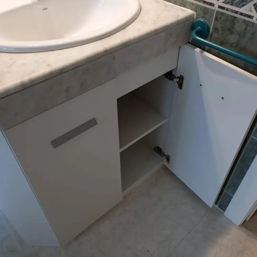 Mueble de baño blanco con puerta abierta, estante y lavabo.