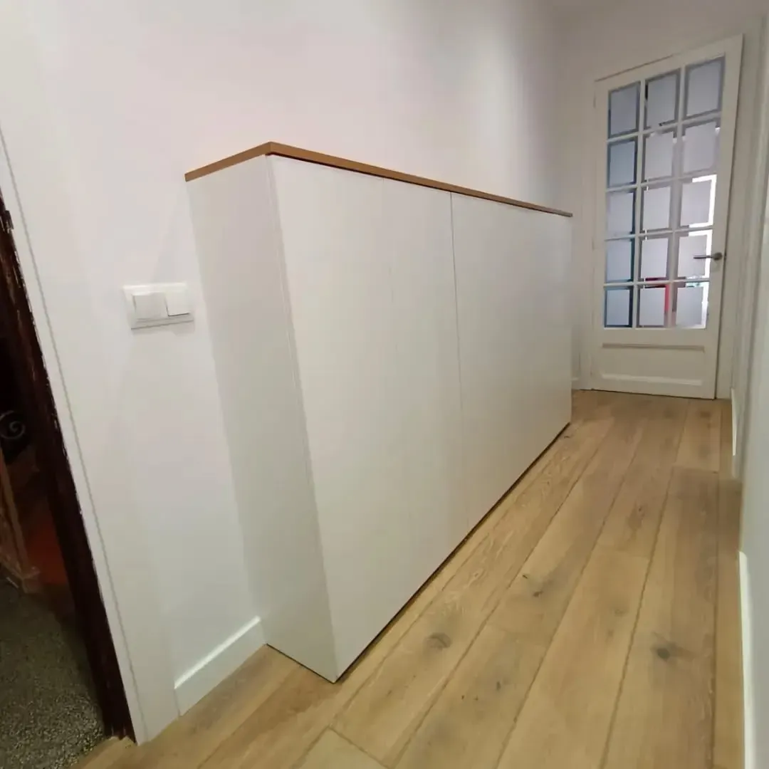 Mueble blanco con tapa de madera en pasillo con suelo de madera y puerta.