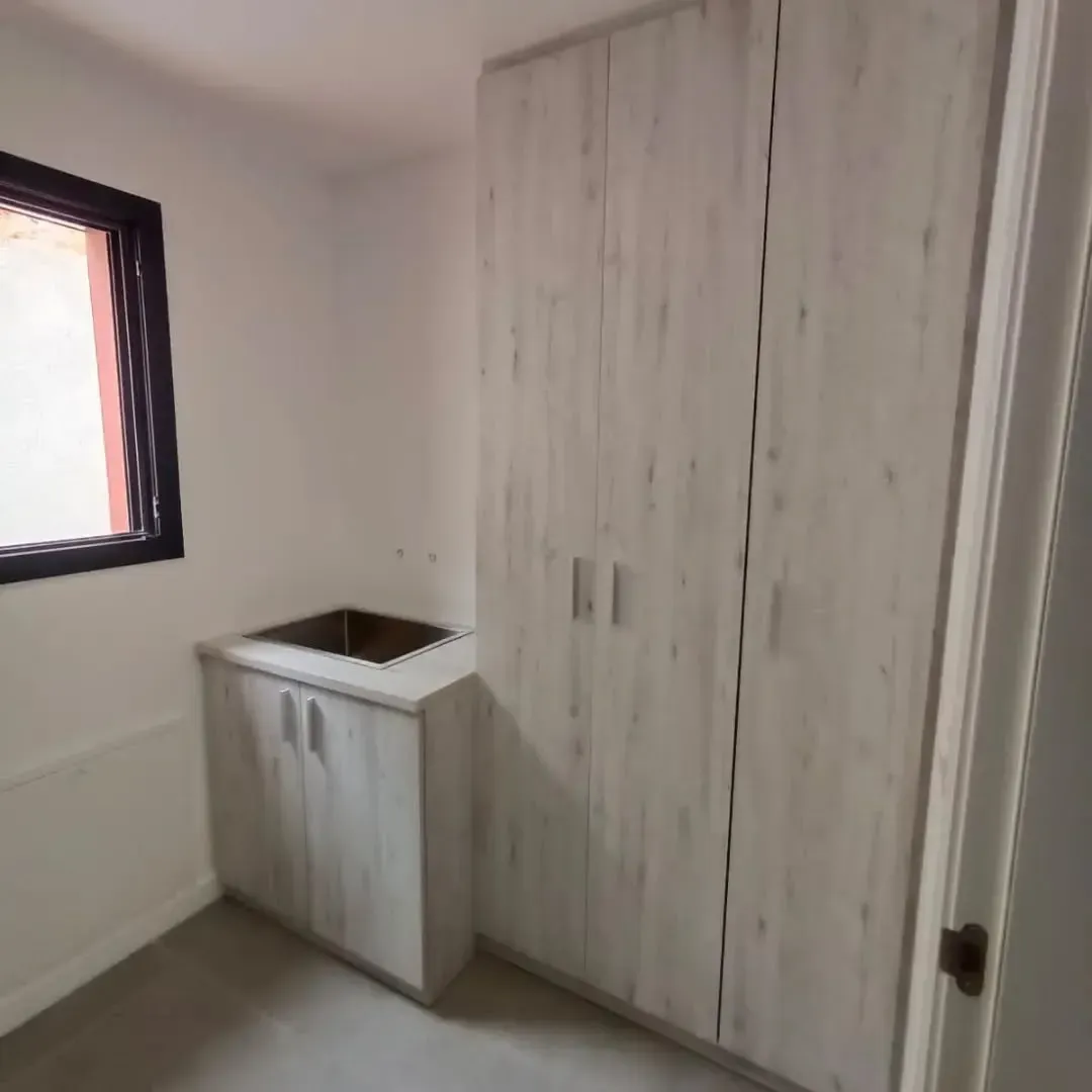 Un pequeño lavadero con mueble y fregadero al lado de un gran armario de madera.