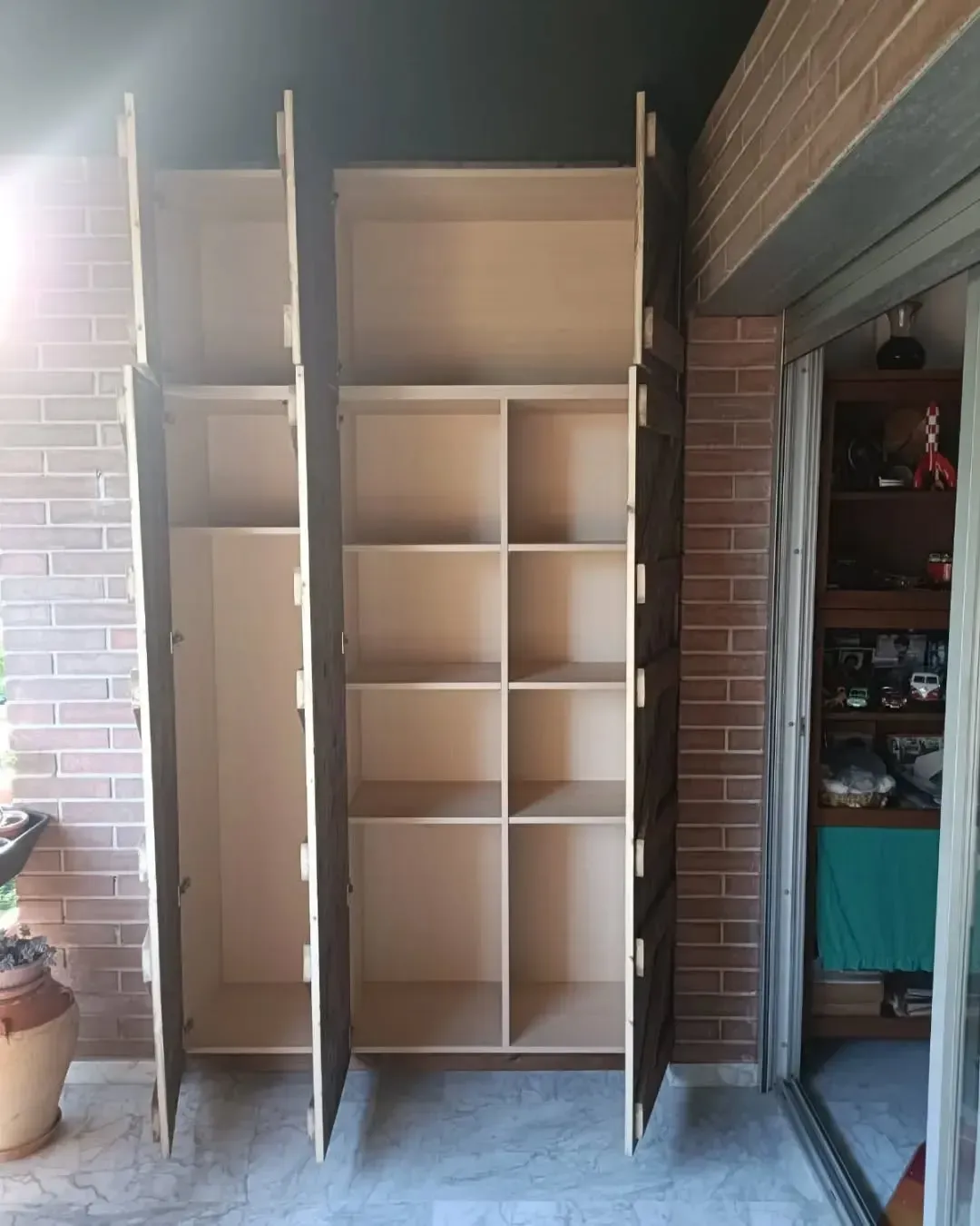 Tres armarios de almacenamiento de madera clara con puertas abiertas contra una pared de ladrillo.