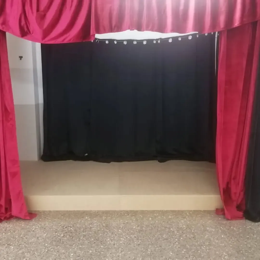 Pequeño escenario con cortinas rojas y fondo negro. Suelo beige.