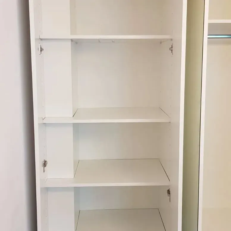 Armario blanco abierto con estantes y dos puertas. Vista interior que muestra tres estantes y espacio.