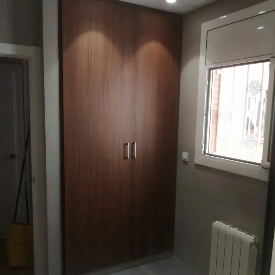 Armario de madera marrón con dos puertas en una habitación, junto a una ventana y un radiador.