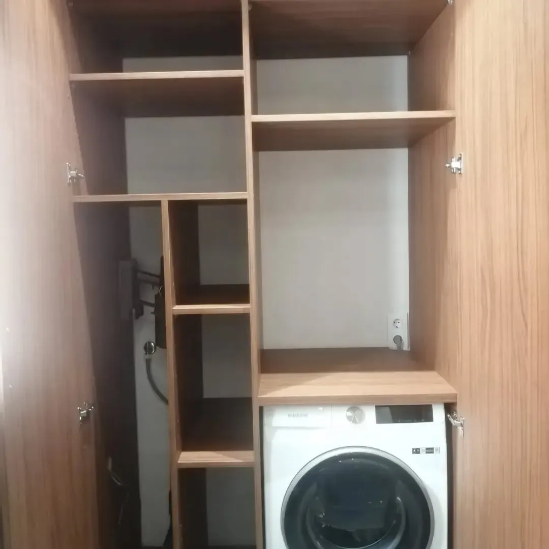 Mueble lavadero de madera con estantes, lavadora incorporada y un pequeño calentador de agua.