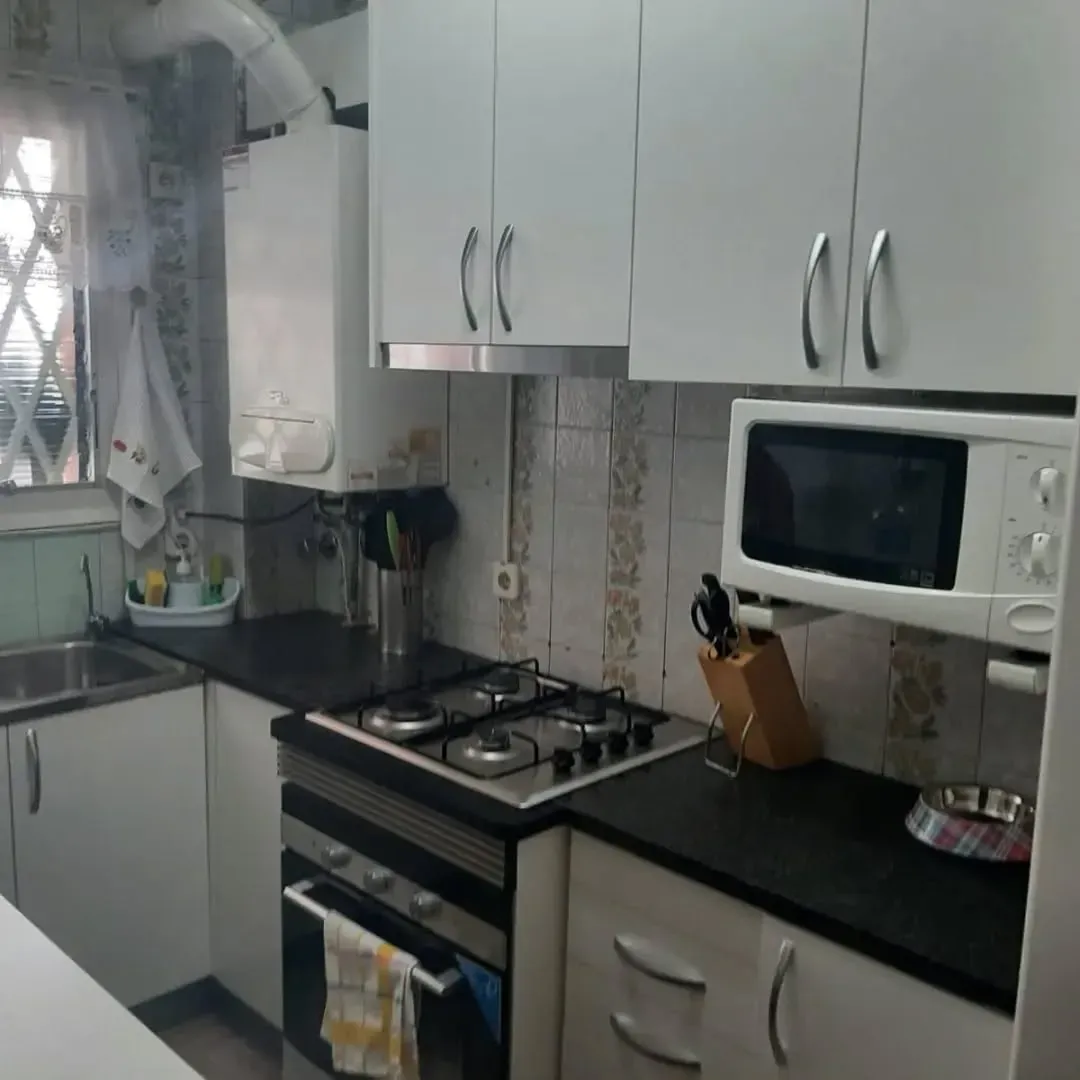 Pequeña cocina blanca con estufa, microondas y gabinetes.