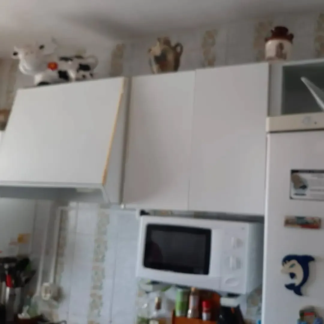 Gabinetes de cocina blancos sobre un microondas y un refrigerador, con elementos decorativos en la parte superior.