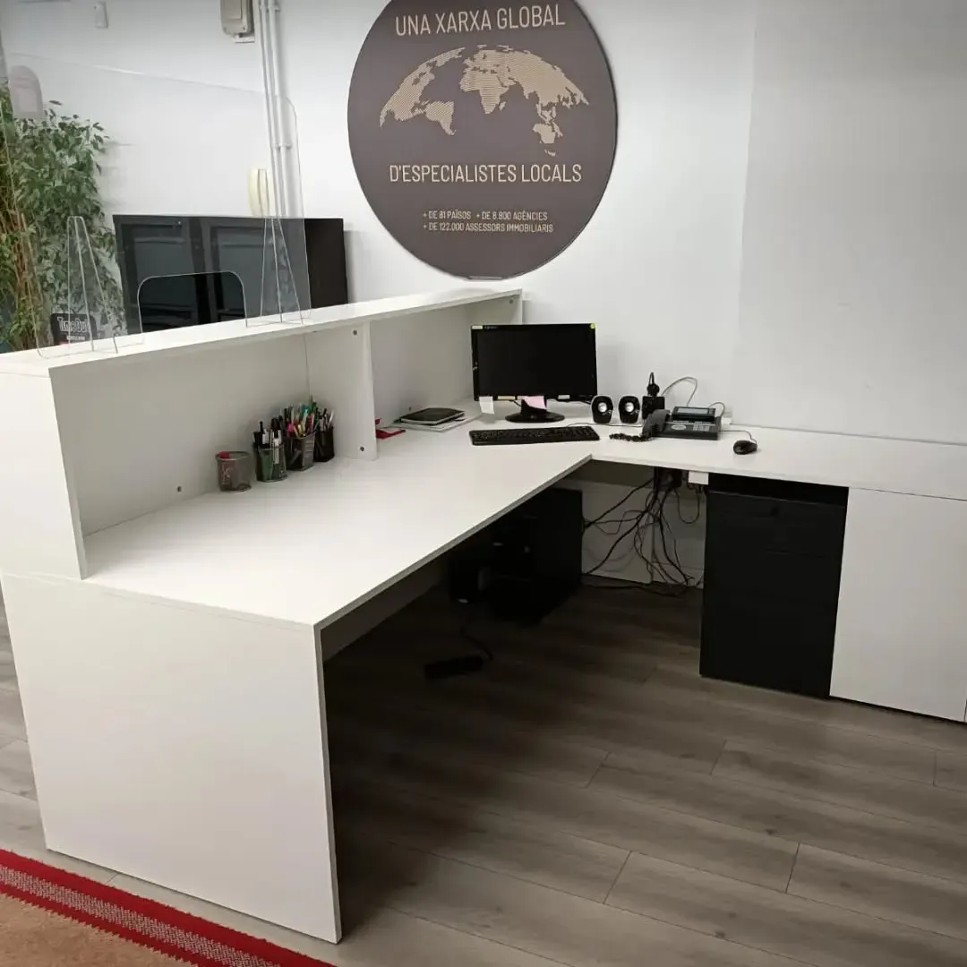 Escritorio de oficina blanco en forma de L con una computadora y suministros, debajo de un cartel con un mapa del mundo.