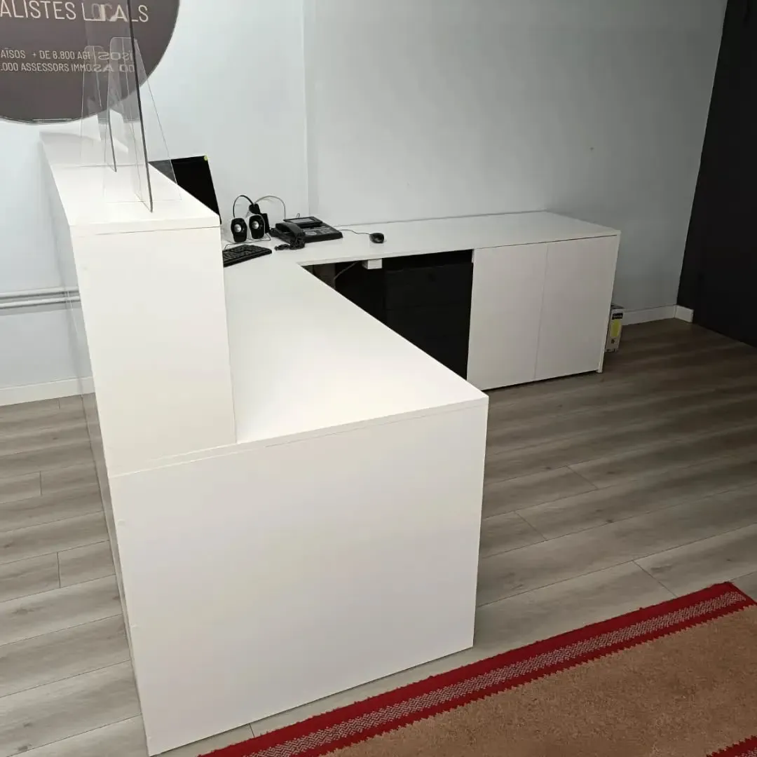 Mostrador de recepción blanco en una oficina esquinera con mampara .