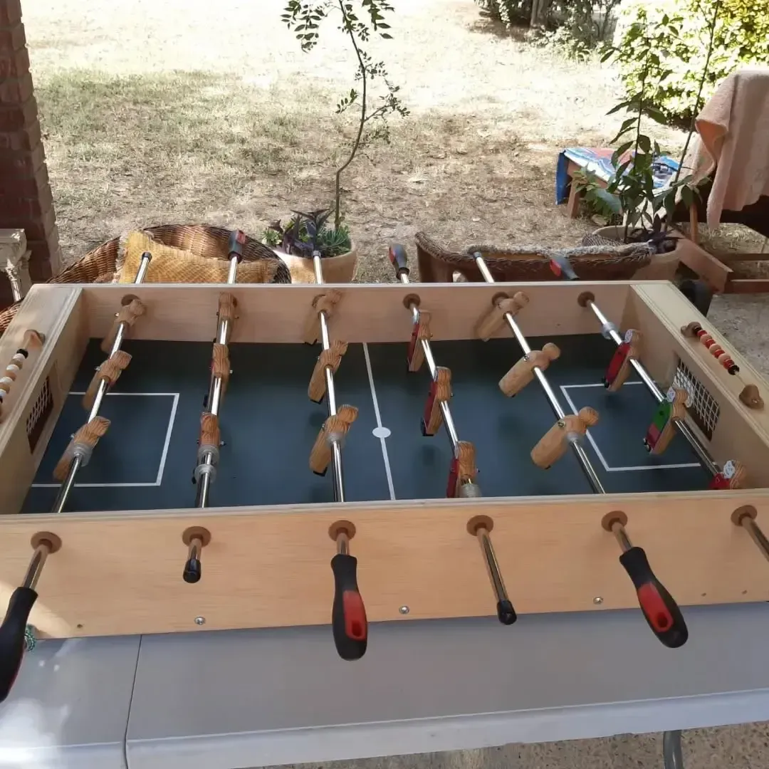 Mesa de futbolín sobre una mesa blanca en un entorno al aire libre con césped y árboles.