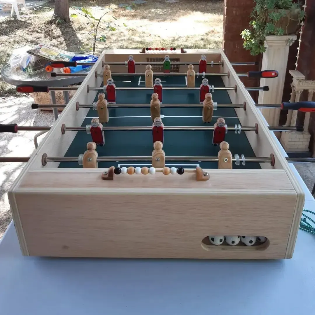 Futbolín de madera clara, listo para jugar. Pelotas y jugadores visibles.