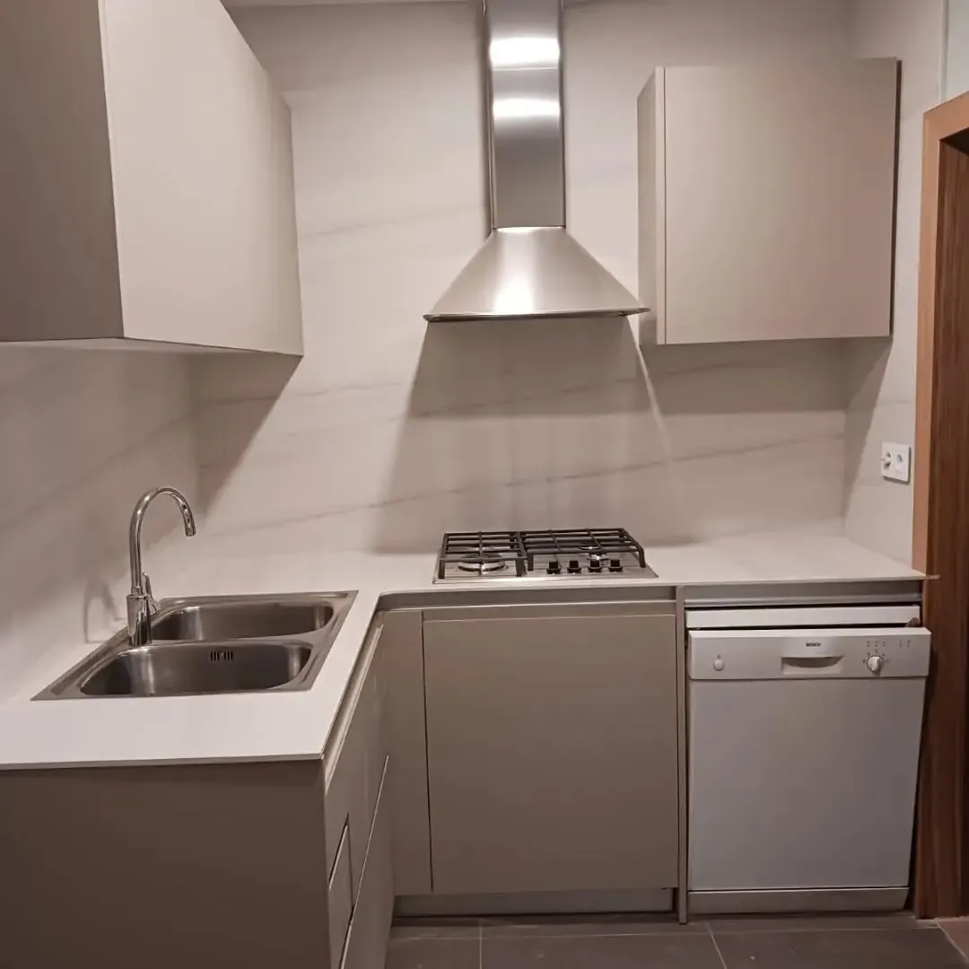 Una cocina pequeña, de tonos neutros, con fregadero, estufa, gabinetes y lavavajillas.