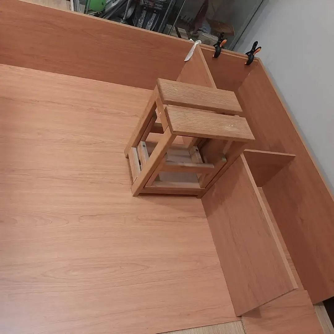 Piezas de muebles de madera en proceso de montaje; incluye una pequeña escalera de madera.