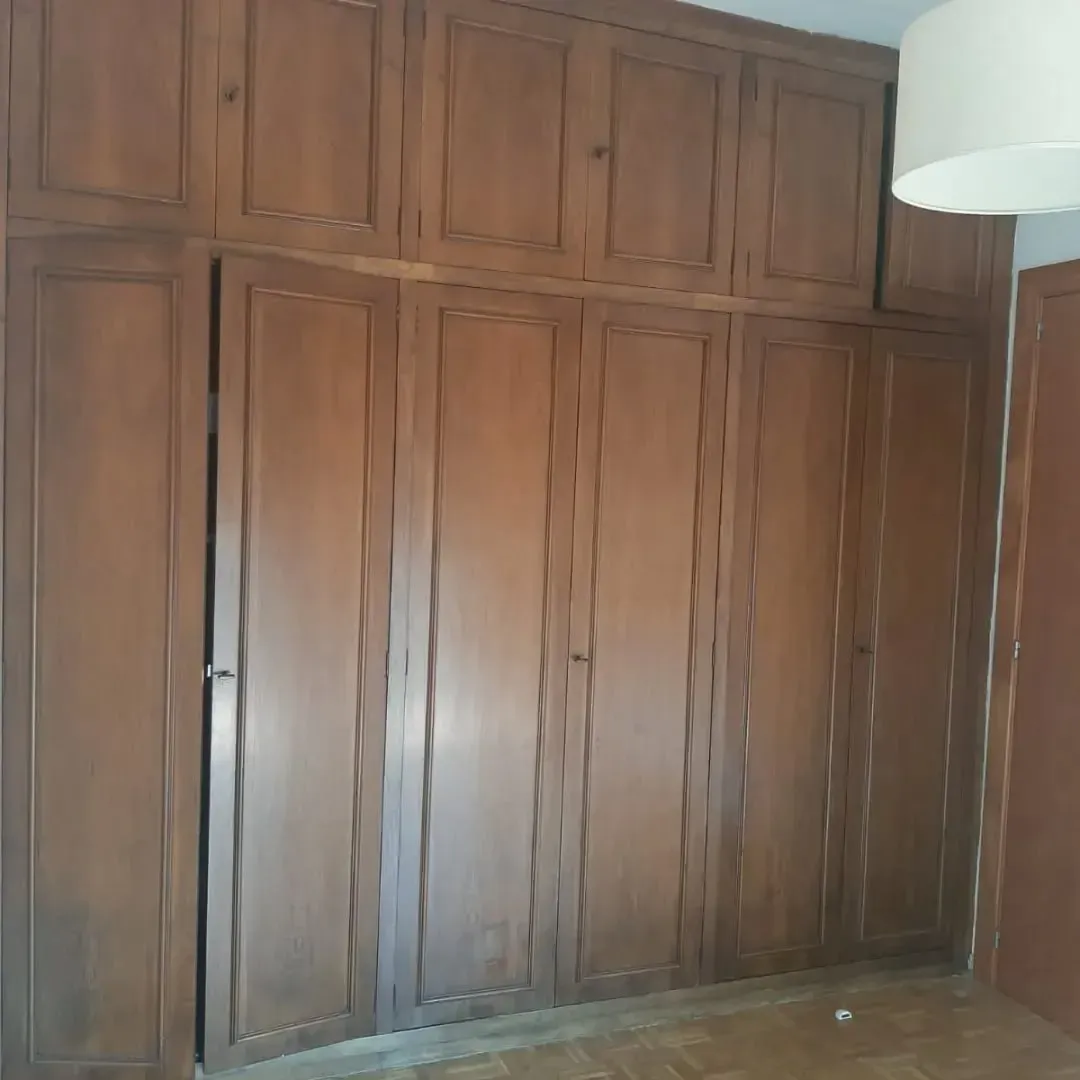 Armario empotrado de madera con varias puertas. Marrón, en una habitación con lámpara y puerta.