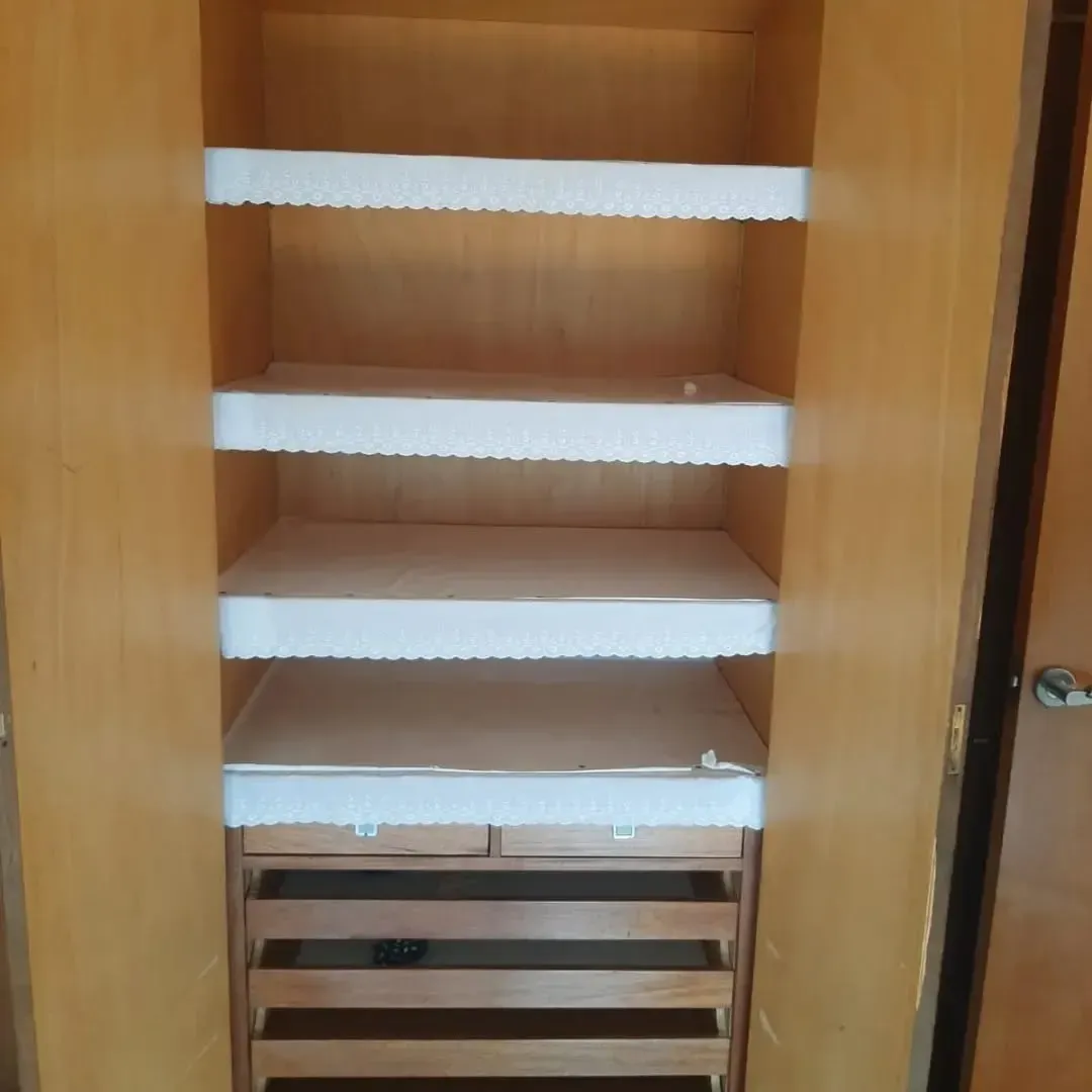 Armario de madera con puertas abiertas, cuatro estantes forrados en tela blanca y cajones debajo.