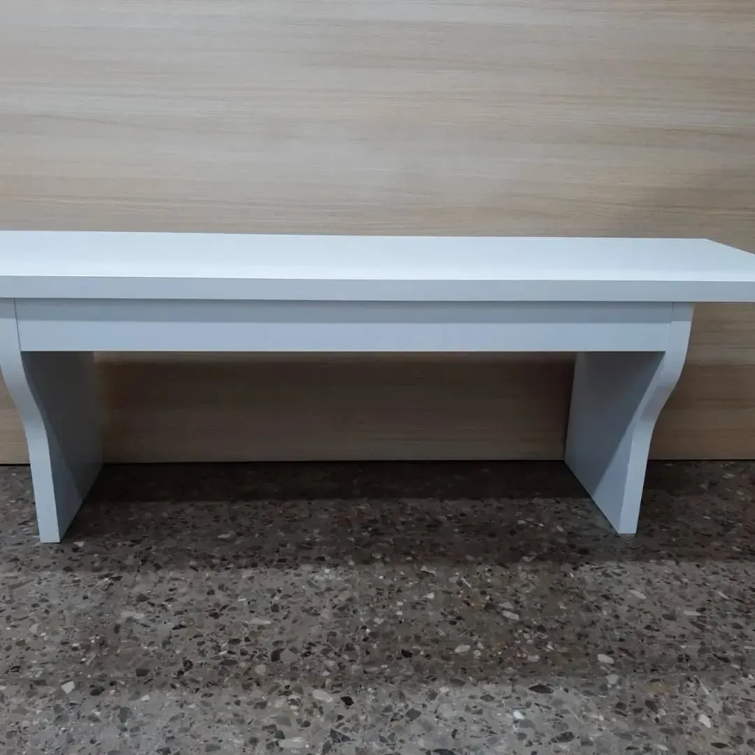 Banco de madera blanca contra una pared de color marrón claro, sobre un suelo gris moteado.