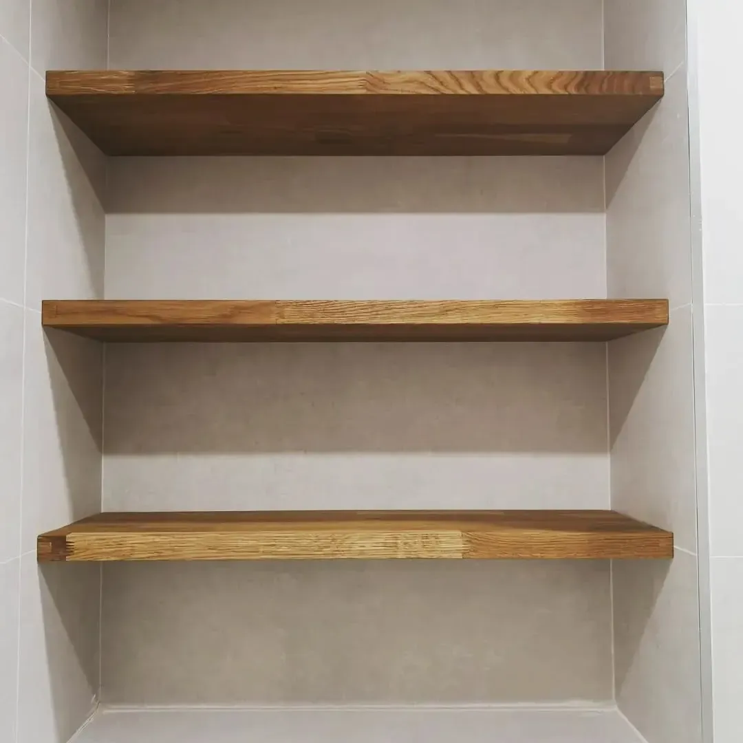 Tres estantes de madera vacíos empotrados en una pared de color neutro.