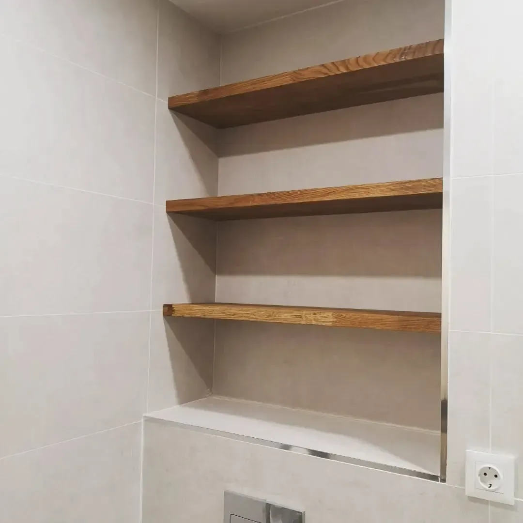 Estantería empotrada con tres baldas de madera en un baño alicatado.