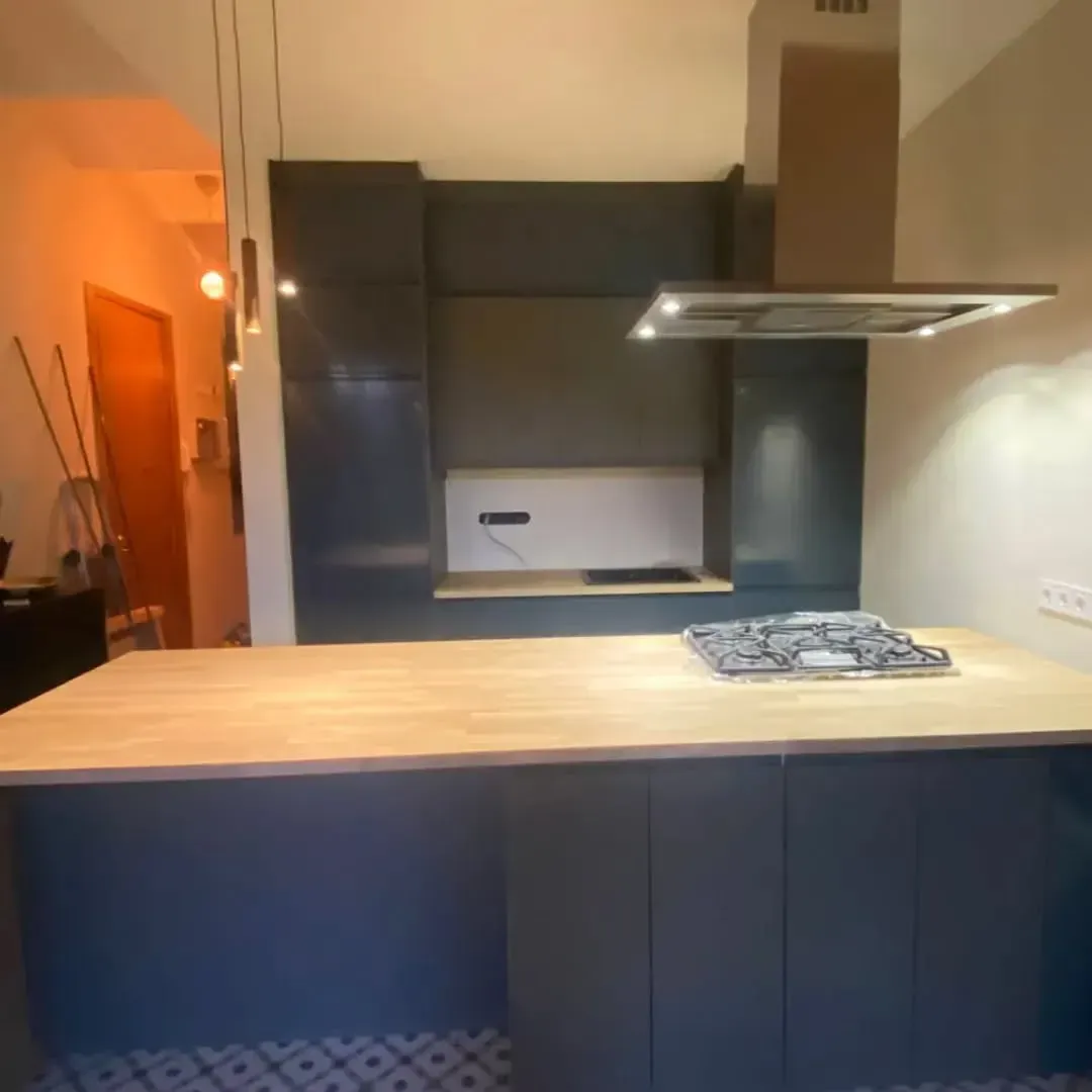 Cocina moderna con isla y gabinetes azules, encimera de madera y estufa.